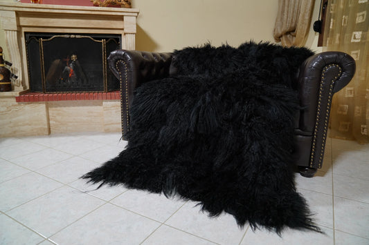 Wool Sheepskin Mongolian Blanket Throw Black - Tatifurs spread across a tufted leather armchair in front of the fireplace, showing the full-skin length and dense black curly pile