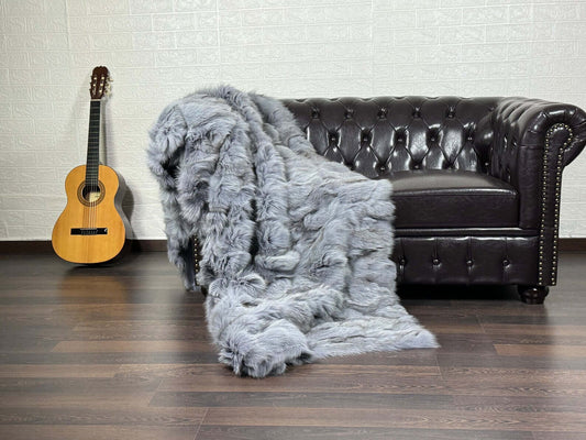 Fox Fur Blanket Throw Bluejean - Tatifurs draped over a stylish couch next to a guitar, showcasing its luxurious texture.