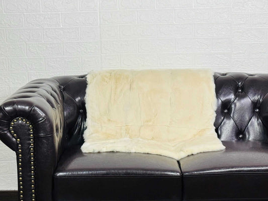 Luxury beige Rex rabbit full skin blanket draped over a linen sofa showing warm organic beige tones and natural pelt flow
