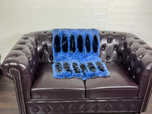 Rex Rabbit Blanket Throw Full Skin Blue Black draped over a brown leather sofa, showcasing its cool blue and wild black spots.