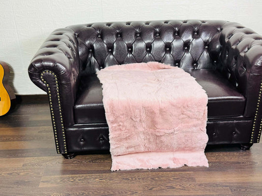 Luxury baby pink Rex rabbit full skin blanket draped over a pale sofa showing soft luminous pink tones and natural pelt flow