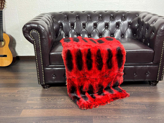 Rex Rabbit Blanket Throw Full Skin Red Black - Tatifurs draped over a leather couch, showcasing vibrant red and black fur.