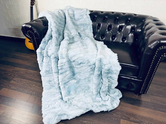 Rabbit Blanket Throw Rex Light Blue - Tatifurs draped over a stylish black leather couch.