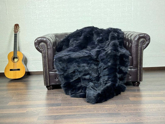 Luxury blue black fox fur blanket draped over a dark sofa showing deep inky blue and black tones