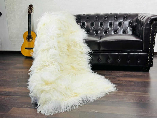 Luxury off white cream Mongolian sheepskin full skin blanket draped over a linen sofa showing warm natural cream tone and extraordinarily long fluffy wool throughout