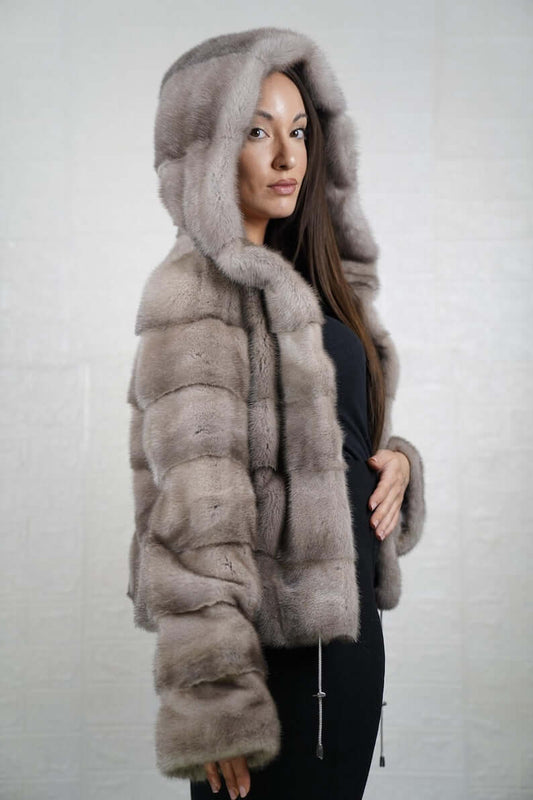 Woman wearing a gray mink fur coat with a hood against a plain background