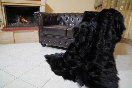 Fox Fur Blanket Throw Black - Tatifurs draped over a leather couch near a fireplace, showcasing its luxurious texture.