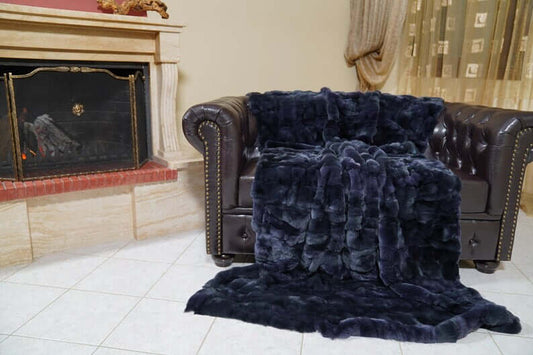 Double Sided Fur Rex Rabbit Blanket Throw Dark Blue draped over a leather sofa near a fireplace.