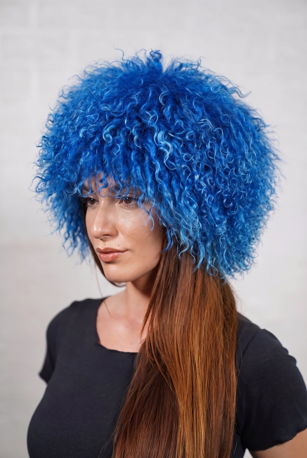 Mongolian Sheepskin Hat Blue — Curly Lamb Fur, One Size — three-quarter view worn by a woman, long curly rich cobalt blue Tibetan lamb fur framing the face, TatiFurs