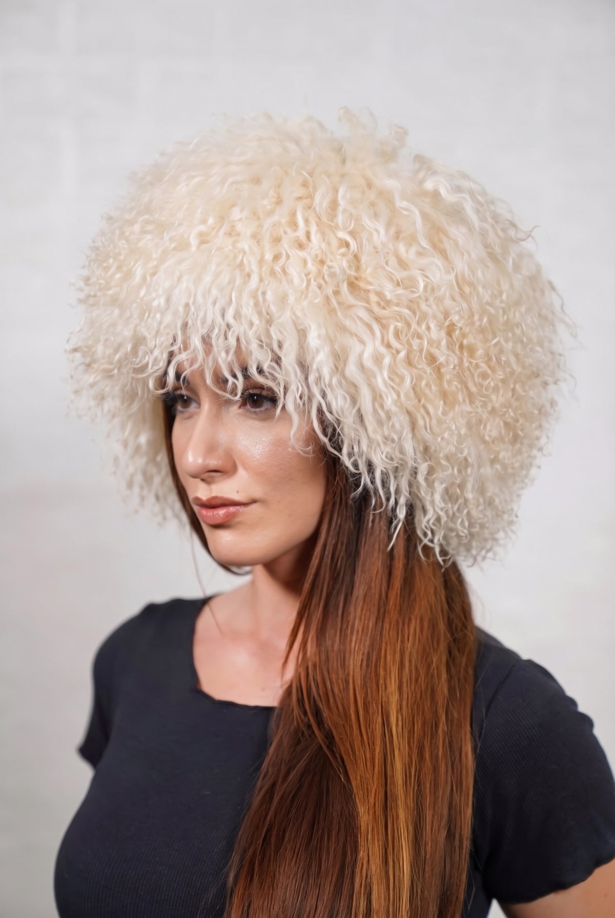 Mongolian Sheepskin Hat Cream Beige — Curly Lamb Fur, One Size — three-quarter view worn by a woman, long curly soft cream beige Tibetan lamb fur framing the face, TatiFurs