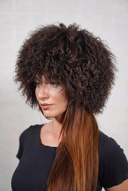 Mongolian Sheepskin Hat Dark Brown — Curly Lamb Fur, One Size — three-quarter view worn by a woman, long curly deep chocolate brown Tibetan lamb fur framing the face, TatiFurs