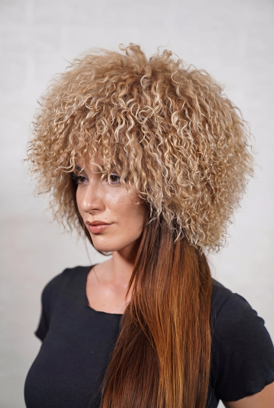 Mongolian Sheepskin Hat Light Brown — Curly Lamb Fur, One Size — three-quarter view worn by a woman, long curly milky caramel light brown Tibetan lamb fur framing the face, TatiFurs
