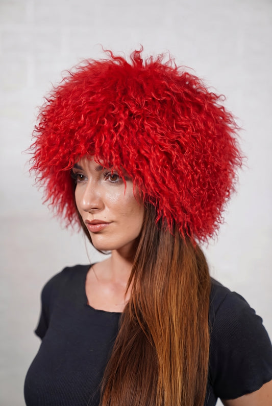 Mongolian Sheepskin Hat Red — Curly Lamb Fur, One Size — three-quarter view worn by a woman, long curly vivid scarlet red Tibetan lamb fur framing the face, TatiFurs
