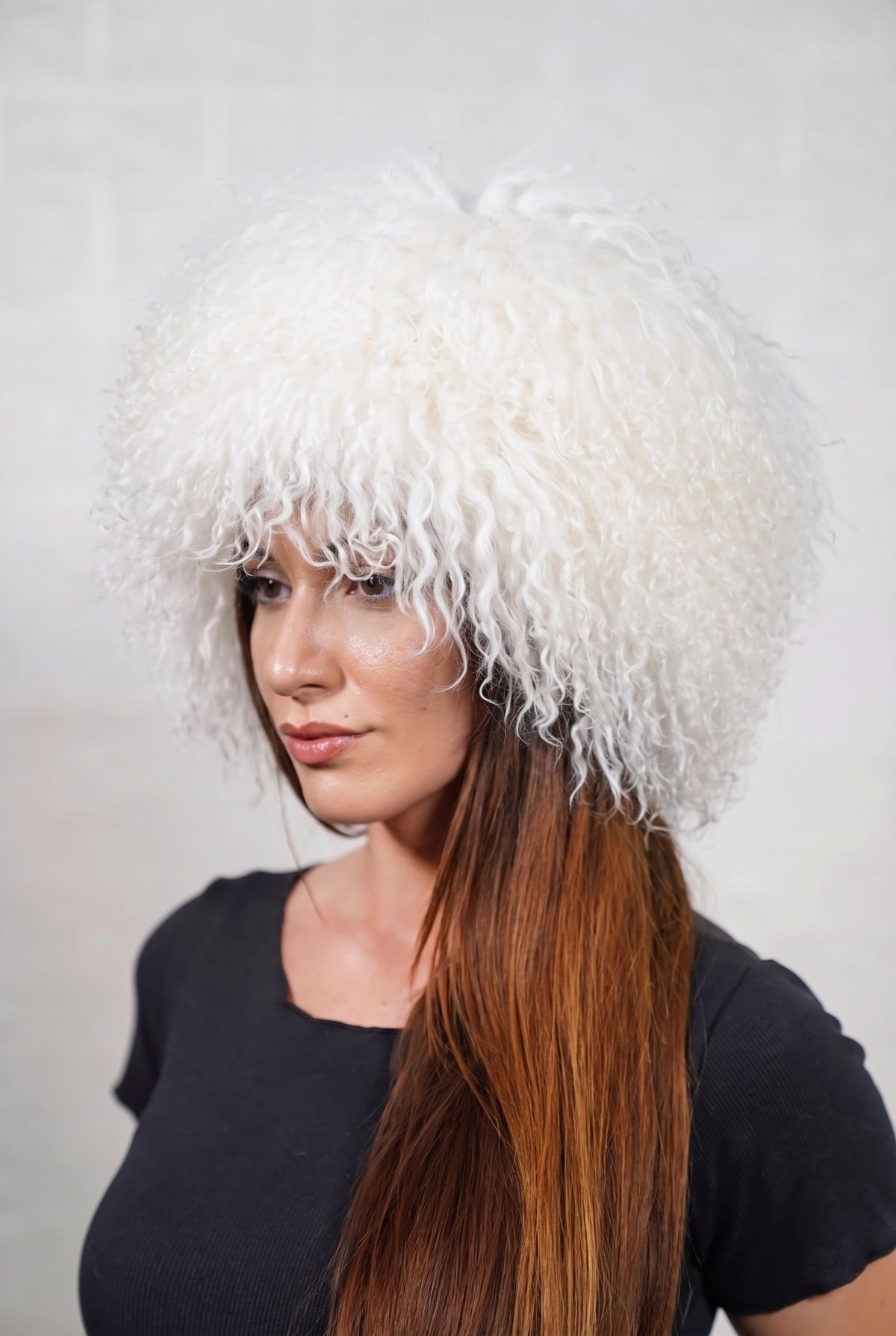 Mongolian Sheepskin Hat White — Curly Lamb Fur, One Size — three-quarter view worn by a woman, long curly pure snow white Tibetan lamb fur framing the face, TatiFurs