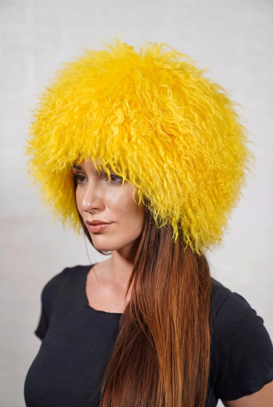 Mongolian Sheepskin Hat Yellow — Curly Lamb Fur, One Size — three-quarter view worn by a woman, long curly warm sunflower yellow Tibetan lamb fur framing the face, TatiFurs