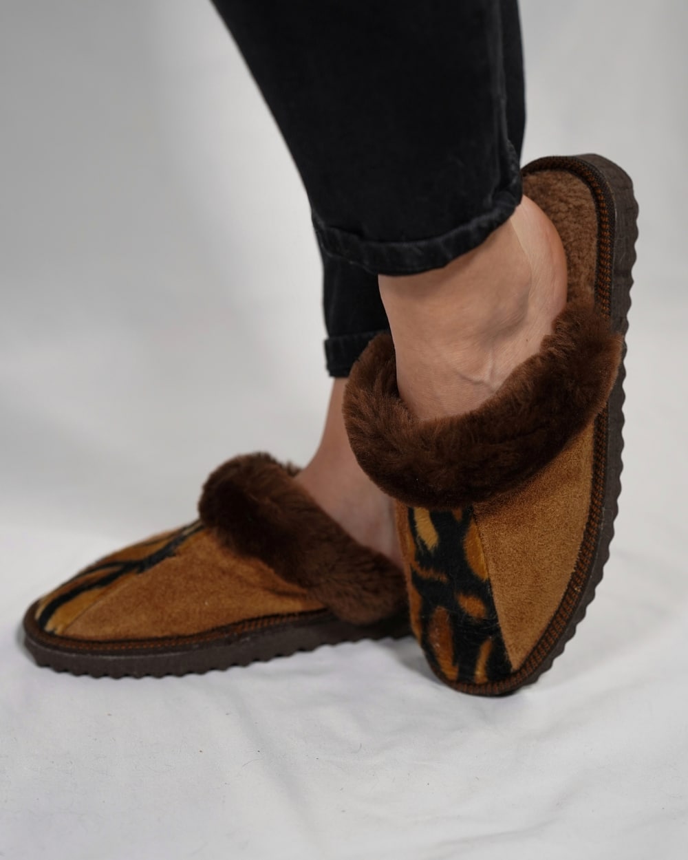 Brown slippers with fuzzy trim worn by a person on a white background