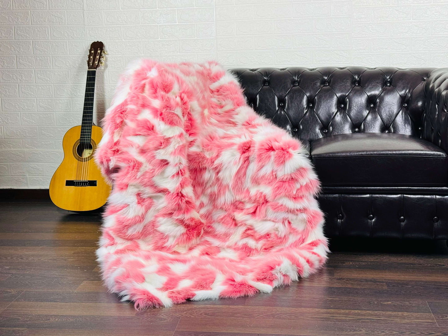 Fox Fur Blanket Throw Pink White - Tatifurs draped on a leather couch next to a guitar, showcasing its soft colors.
