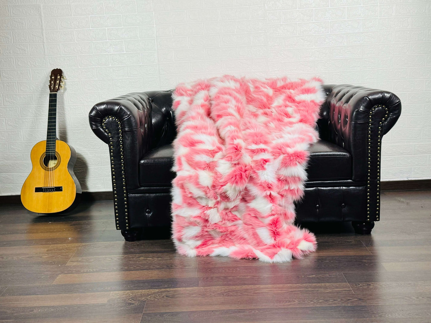 Fox Fur Blanket Throw Pink White - Tatifurs draped on a black leather couch with a guitar in the background.