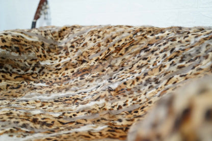 rabbit fur throw blanket leopard print — folded over armchair, flowing pile wild pattern visible — Greek craftsmanship, TatiFurs
