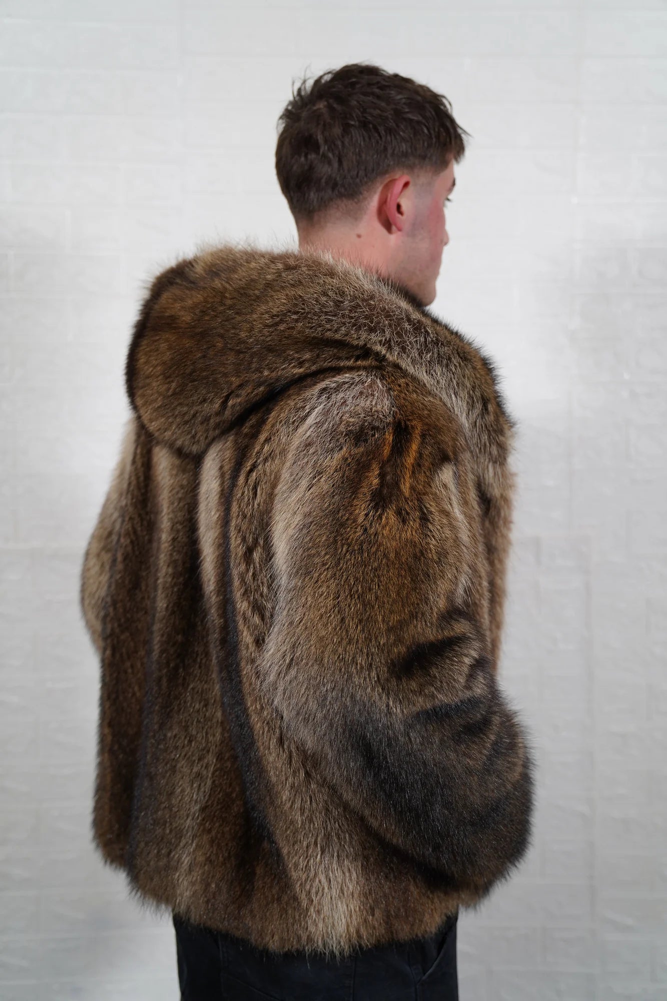 Raccoon fur jacket men natural brown hood worn up showing velvet lined hood interior framing face against dramatic natural brown raccoon exterior — Greek craftsmanship, TatiFurs
