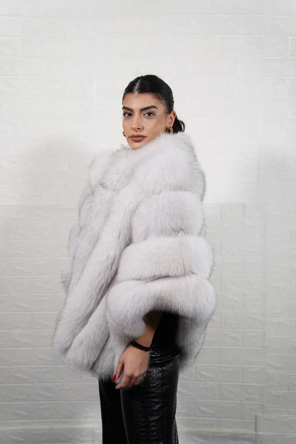 Fox fur poncho blue natural shown from the side displaying hip level poncho silhouette and luminous natural blue fox horizontal rows with rabbit trim — Greek craftsmanship, TatiFurs
