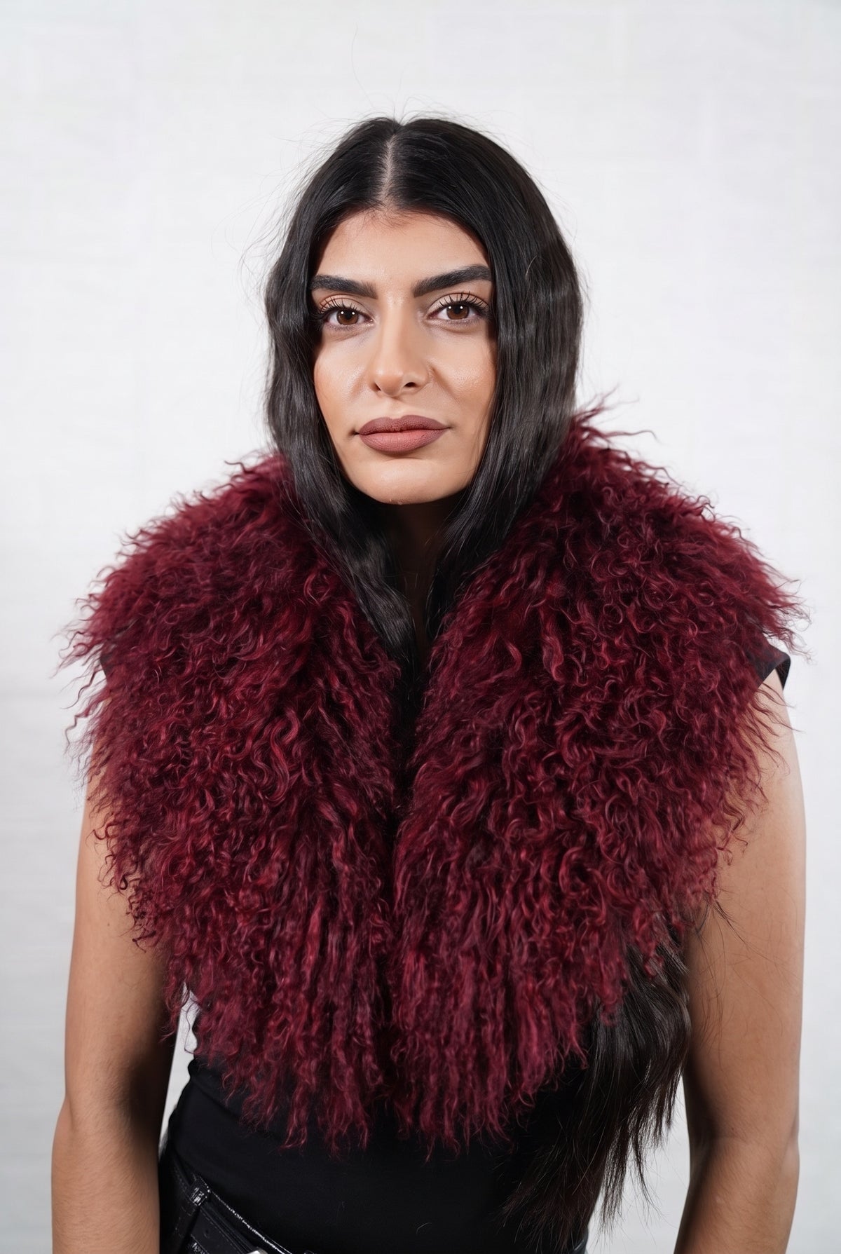 Mongolian Sheepskin Collar Burgundy — Curly Lamb Fur worn by a woman, front view of the long curly deep oxblood burgundy Tibetan lamb fur framing the face and shoulders, TatiFurs