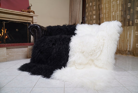 Mongolian Blanket Throw Black White Two Tone — Wool Sheepskin draped over a dark brown leather Chesterfield sofa beside a lit fireplace — full view of the jet black and pure white long curly wool, TatiFurs
