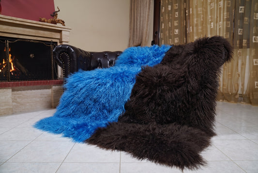 Mongolian Blanket Throw Blue Dark Brown Two Tone — Wool Sheepskin draped over a dark brown leather Chesterfield sofa beside a lit fireplace — full view of the cobalt blue and espresso brown long curly wool, TatiFurs