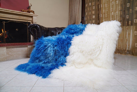 Mongolian Blanket Throw Blue White Two Tone — Wool Sheepskin draped over a dark brown leather Chesterfield sofa beside a lit fireplace — full view of the cobalt blue and pure white long curly wool, TatiFurs