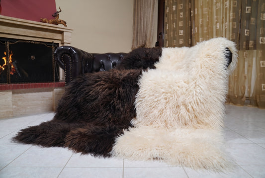 Mongolian Blanket Throw Dark Brown Cream Beige Two Tone draped over a dark brown leather Chesterfield sofa beside a lit fireplace — full view of the espresso brown and cream beige long curly wool, TatiFurs
