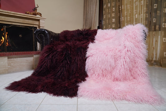 Mongolian Blanket Throw Dark Burgundy Pink Two Tone — Wool Sheepskin draped over a dark brown leather Chesterfield sofa beside a lit fireplace — full view of the deep burgundy and powder pink long curly wool, TatiFurs
