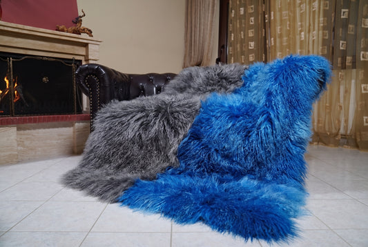 Mongolian Blanket Throw Grey Blue Two Tone — Wool Sheepskin draped over a dark brown leather Chesterfield sofa beside a lit fireplace — full view of the charcoal grey and cobalt blue long curly wool, TatiFurs