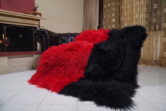 Mongolian Blanket Throw Red Black Two Tone — Wool Sheepskin draped over a dark brown leather Chesterfield sofa beside a lit fireplace — full view of the scarlet red and jet black long curly wool, TatiFurs
