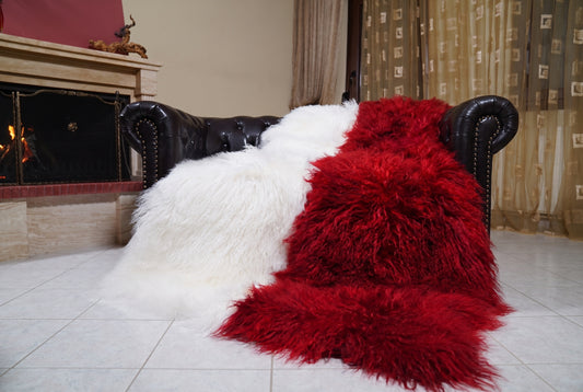 Mongolian Blanket Throw White Red Two Tone — Wool Sheepskin draped over a dark brown leather Chesterfield sofa beside a lit fireplace — full view of the pure white and scarlet red long curly wool, TatiFurs