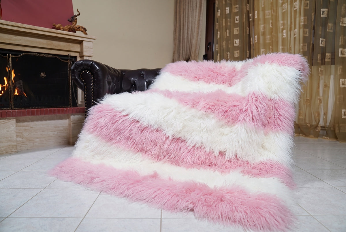 Mongolian Blanket Throw Pink White Striped — Wool Sheepskin draped over a dark brown leather Chesterfield sofa beside a lit fireplace — full view of the powder pink and pure white long curly wool, TatiFurs