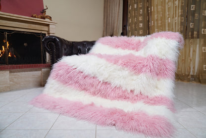 Mongolian Blanket Throw Pink White Striped — Wool Sheepskin draped over a dark brown leather Chesterfield sofa beside a lit fireplace — full view of the powder pink and pure white long curly wool, TatiFurs