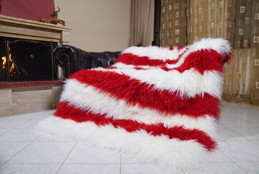 Mongolian Blanket Throw White Red Striped — Wool Sheepskin draped over a dark brown leather Chesterfield sofa beside a lit fireplace — full view of the pure white and scarlet red long curly wool, TatiFurs