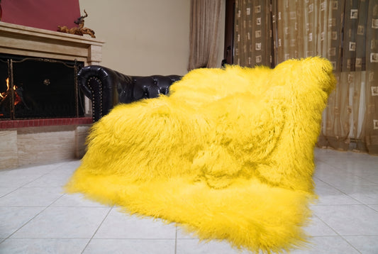 Mongolian Blanket Throw Yellow — Wool Sheepskin Full Skin draped over a dark brown leather Chesterfield sofa beside a lit fireplace — full view of the bright sunny yellow long curly wool, TatiFurs
