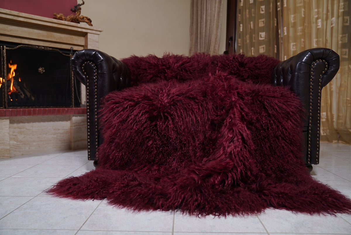 Mongolian Blanket Throw Burgundy — Wool Sheepskin Full Skin spread across the leather sofa showing the whole deep oxblood burgundy Mongolian wool surface — Greek craftsmanship, TatiFurs