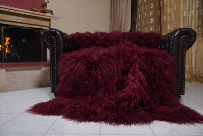 Mongolian Blanket Throw Burgundy — Wool Sheepskin Full Skin spread across the leather sofa showing the whole deep oxblood burgundy Mongolian wool surface — Greek craftsmanship, TatiFurs