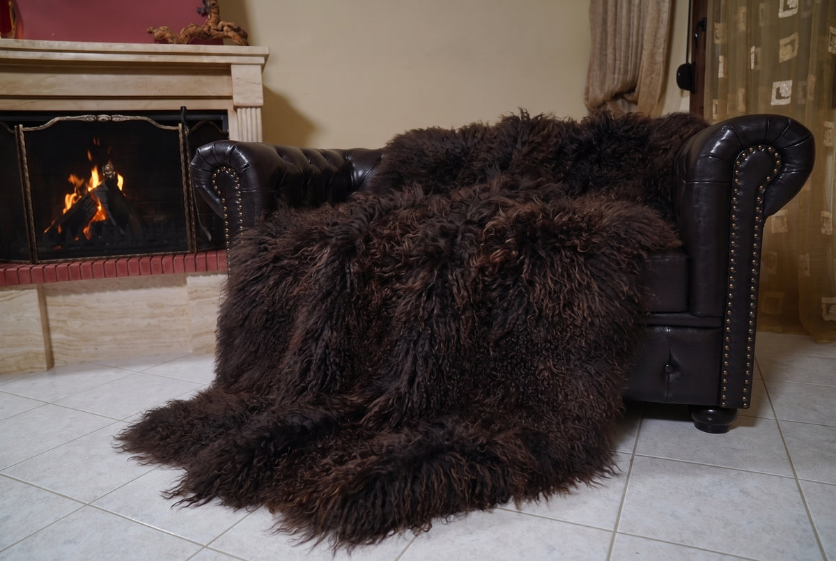 Mongolian Blanket Throw Dark Brown — Wool Sheepskin Full Skin angled view on the Chesterfield sofa with the fire glowing behind — deep espresso dark brown full skin sheepskin, TatiFurs