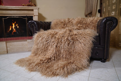 Mongolian Blanket Throw Light Brown — Wool Sheepskin Full Skin angled view on the Chesterfield sofa with the fire glowing behind — milky caramel light brown full skin sheepskin, TatiFurs