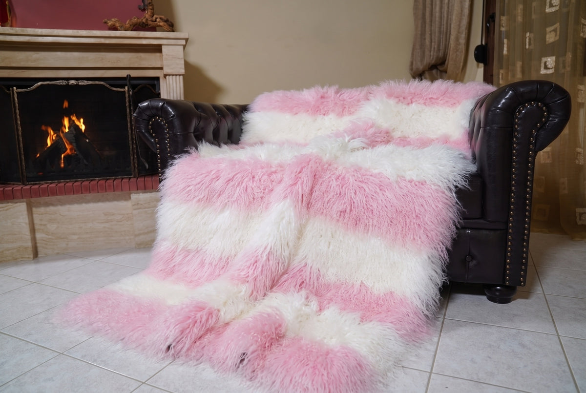 Mongolian Blanket Throw Pink White Striped — Wool Sheepskin angled view on the Chesterfield sofa with the fire glowing behind — powder pink and pure white full skin sheepskin, TatiFurs