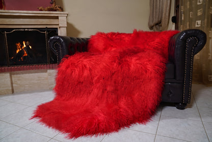 Mongolian Blanket Throw Red — Wool Sheepskin Full Skin angled view on the Chesterfield sofa with the fire glowing behind — vivid scarlet red full skin sheepskin, TatiFurs