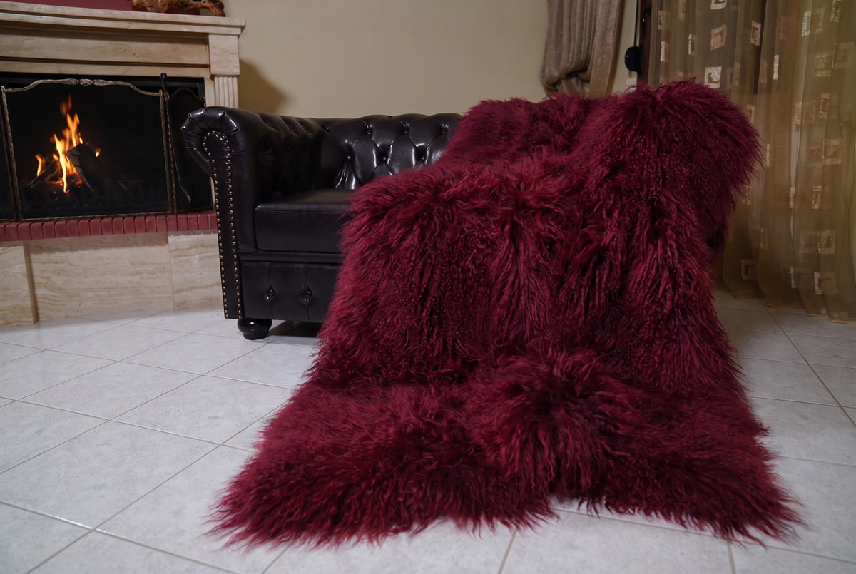 Mongolian Blanket Throw Burgundy — Wool Sheepskin Full Skin draped from the sofa towards the fireplace showing how the deep oxblood burgundy long wool falls — TatiFurs