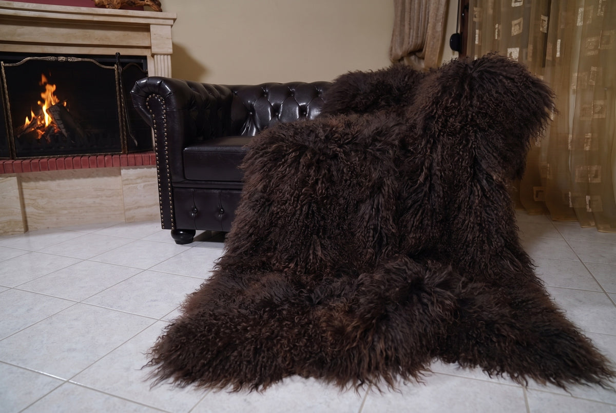 Mongolian Blanket Throw Dark Brown — Wool Sheepskin Full Skin draped from the sofa towards the fireplace showing how the deep espresso dark brown long wool falls — TatiFurs