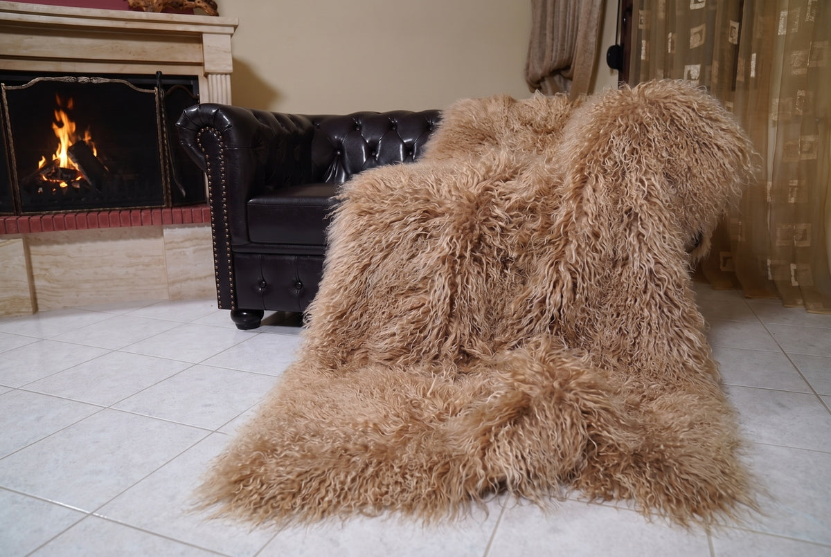 Mongolian Blanket Throw Light Brown — Wool Sheepskin Full Skin draped from the sofa towards the fireplace showing how the milky caramel light brown long wool falls — TatiFurs