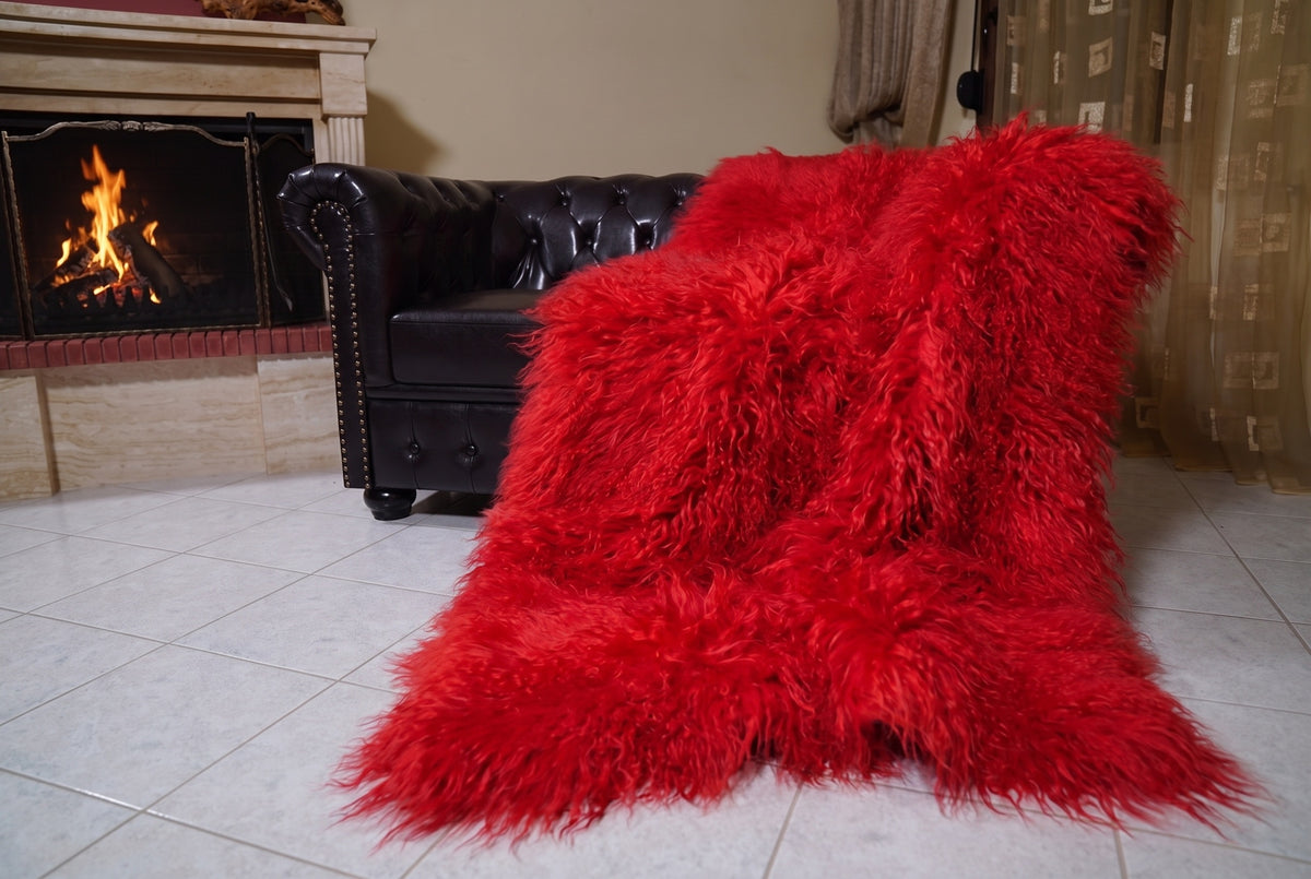 Mongolian Blanket Throw Red — Wool Sheepskin Full Skin draped from the sofa towards the fireplace showing how the vivid scarlet red long wool falls — TatiFurs