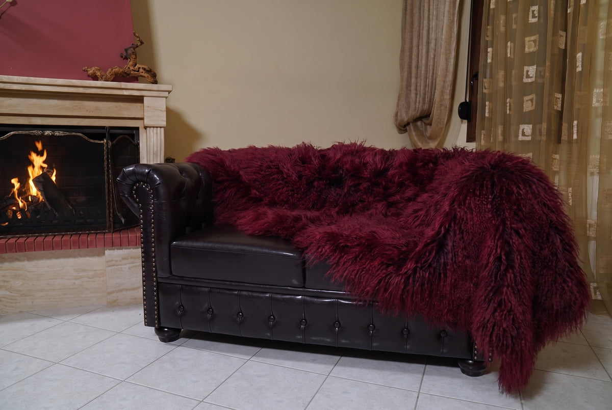Mongolian Blanket Throw Burgundy — Wool Sheepskin Full Skin hanging from the sofa down to the travertine floor — deep oxblood burgundy Mongolian sheepskin throw, TatiFurs