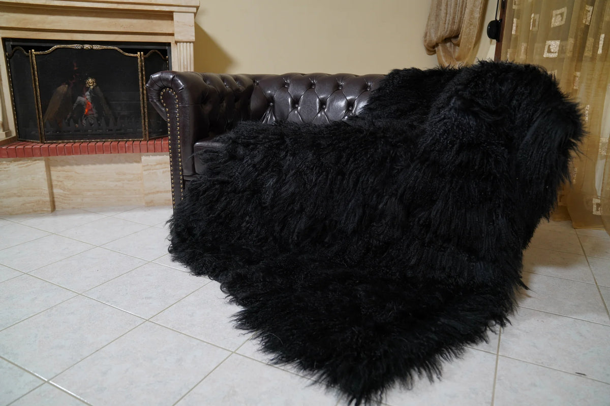 Wool Sheepskin Mongolian Blanket Throw Black - Tatifurs draped over a dark brown Chesterfield leather sofa beside a lit fireplace, long curly black Mongolian wool spilling onto the tiled floor